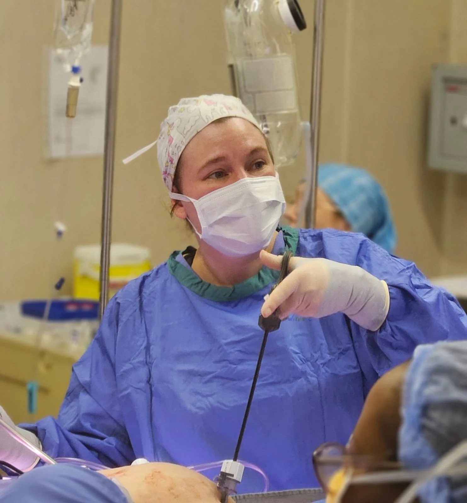 A healthcare professional in surgical scrubs, mask, and gloves performing or assisting in a medical procedure in an operating room.