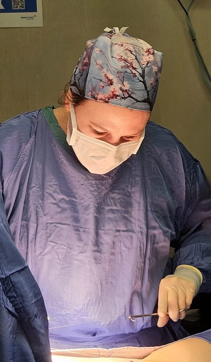A female surgeon in scrubs, a surgical cap with a cherry blossom pattern, and a face mask, performing a surgery in an operating room.