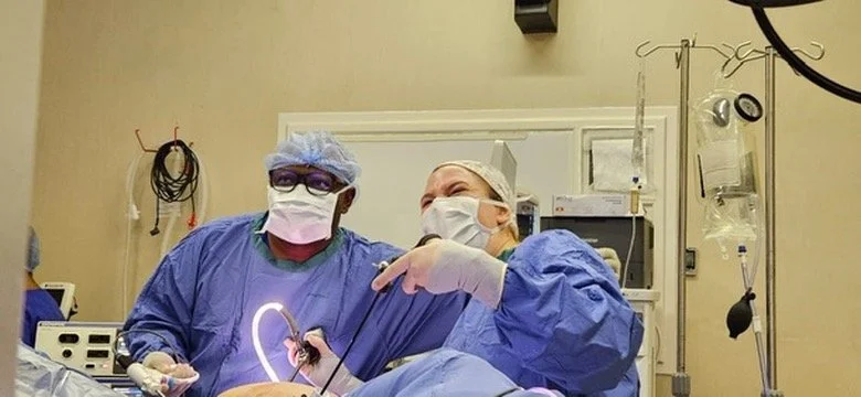 Two medical professionals in scrubs and masks performing surgery in an operating room.