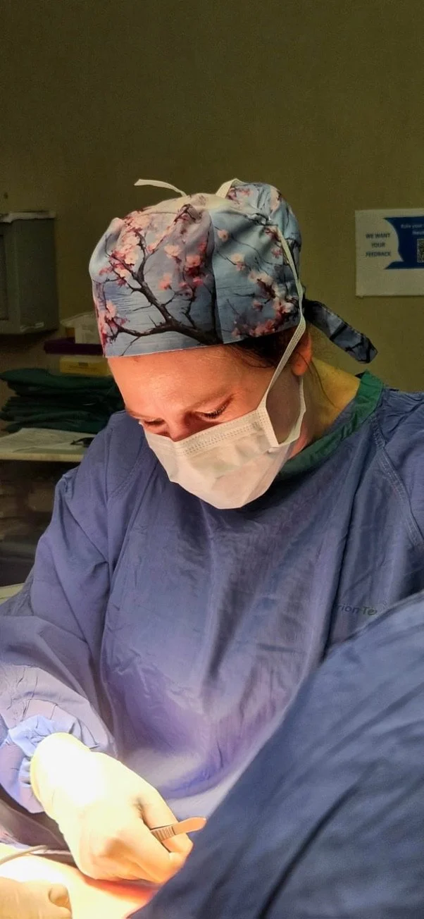 A female healthcare worker dressed in surgical scrubs, a floral-patterned surgical cap, and a face mask performing a medical procedure.