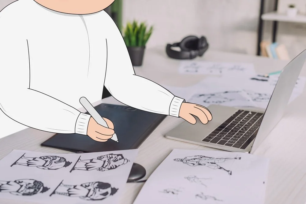 Digital artist sketching fashion figures on a graphics tablet at a desk with a laptop and fashion sketches.