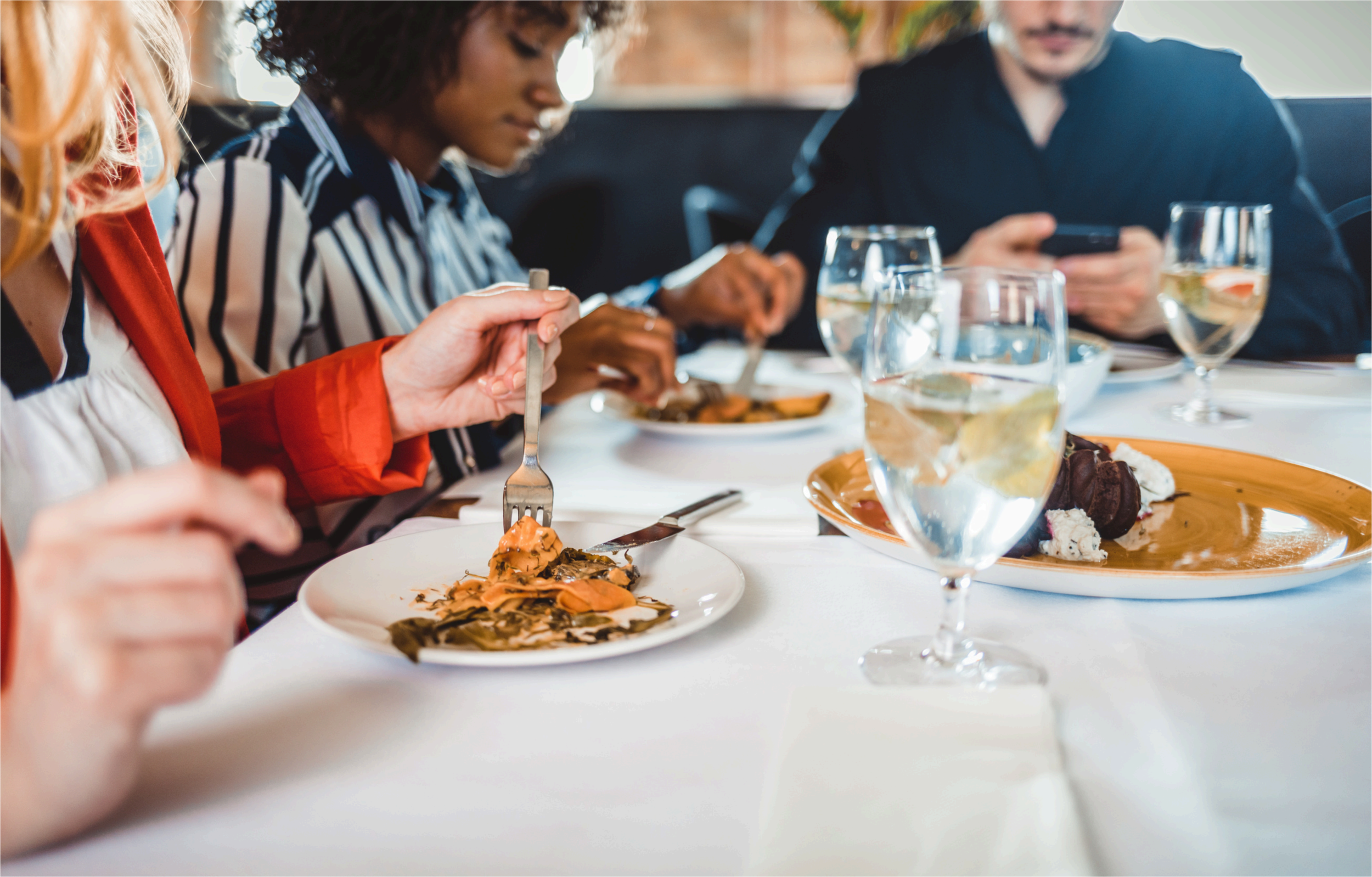 Groupe de personnes dégustant un repas dans un restaurant, avec des verres de vin blanc sur la table.
