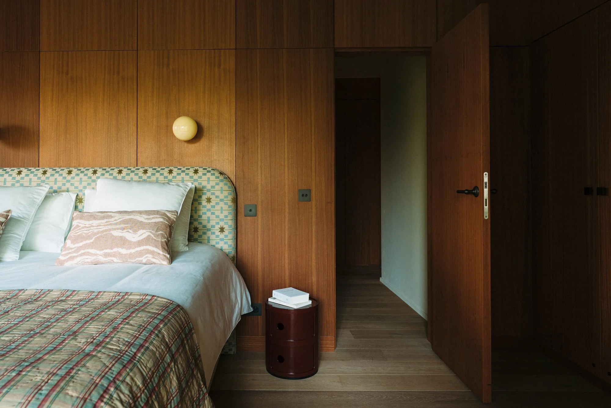 Close-up of a bedroom with a bed, pillows, bedside table with books, and wooden wall panels.