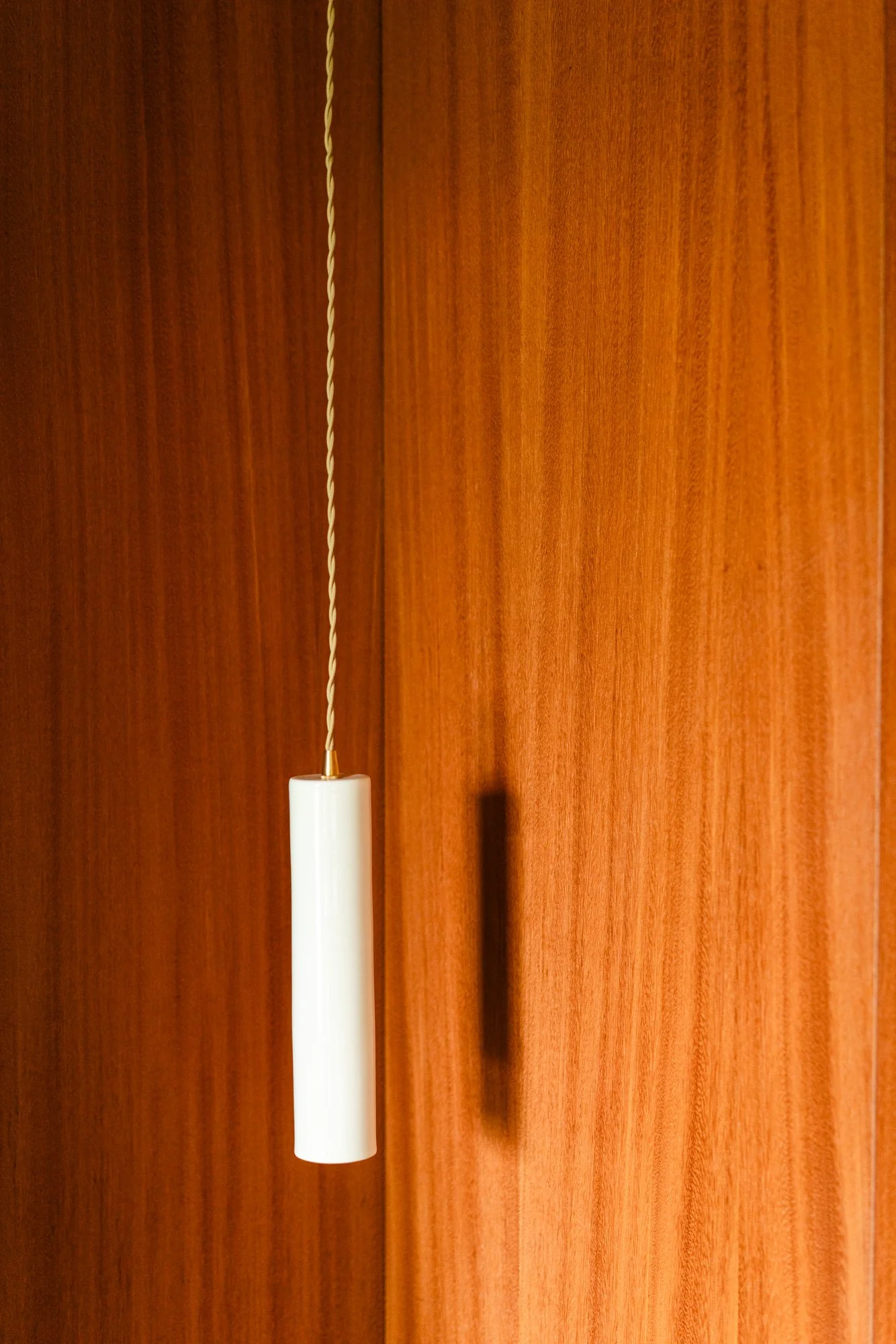 Close-up of a white pendant lamp hanging from a twisted cord against a wooden wall background.