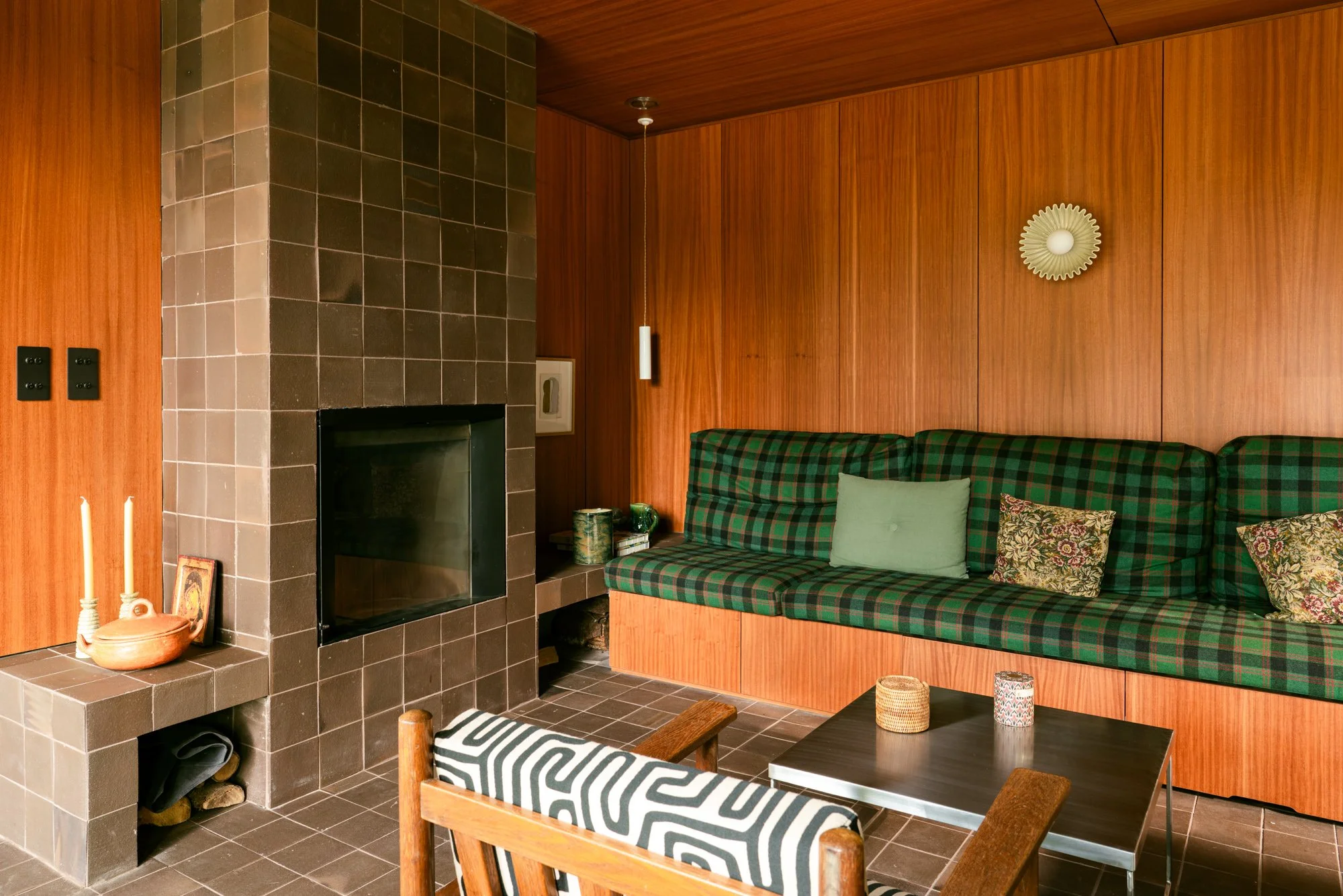 Living room with wood-paneled wall, plaid sofa with decorative pillows, and a fireplace with a tiled surround.