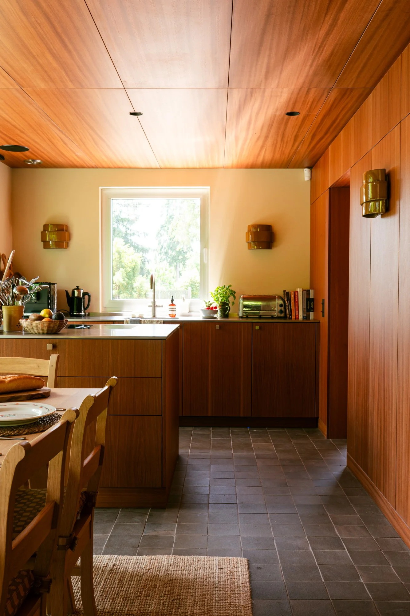 Wood-paneled kitchen with a window, dining table with chairs, and a dark tiled floor.
