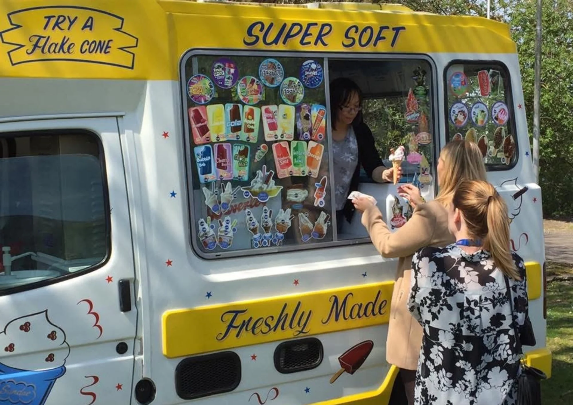 An ice cream truck selling various ice cream treats with three women ordering and receiving ice cream.