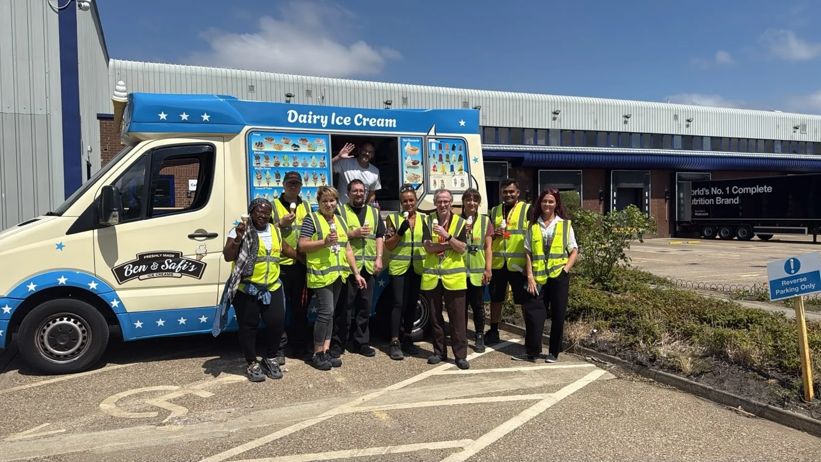 Group of people wearing yellow safety vests standing in front of a Ben & Safi's ice cream truck outdoors, on a sunny day.