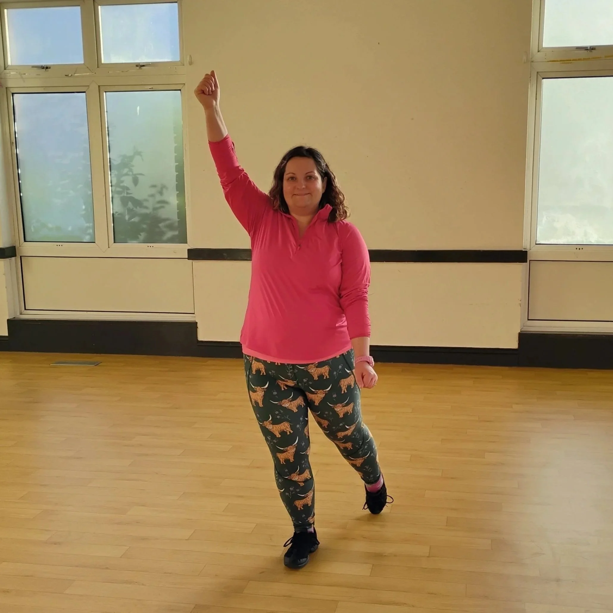 fat, white, female fitness instructor smiling with one arm raised