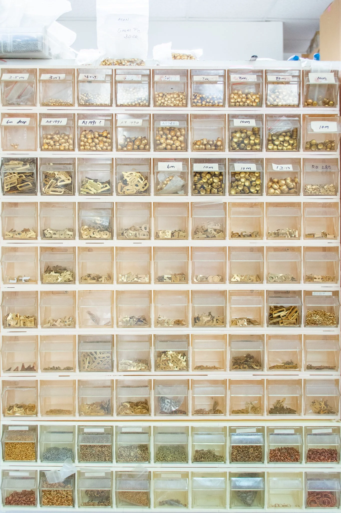 Organized storage of gold-colored hardware, including screws, washers, and brackets in plastic containers with labels.