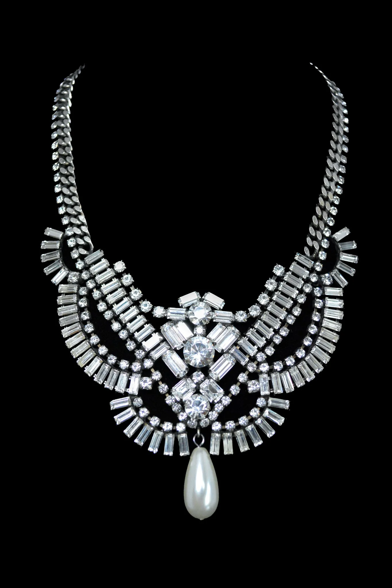 Sparkling diamond necklace with multiple tiers of clear stones and a large pearl pendant, set against a black background.