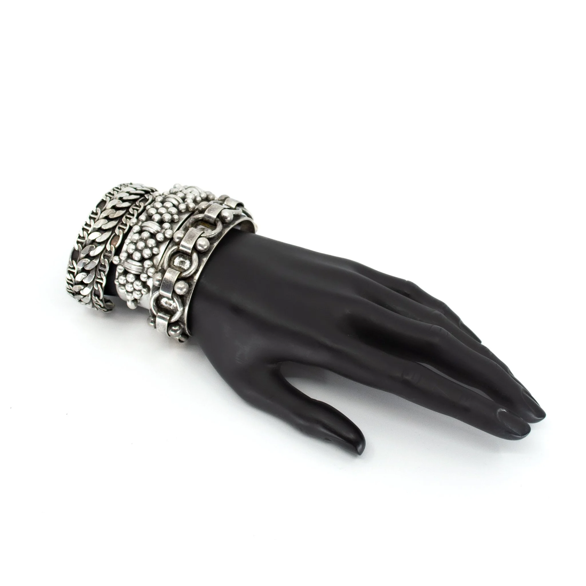 Black mannequin hand wearing multiple silver bracelets with various chain and bead designs.