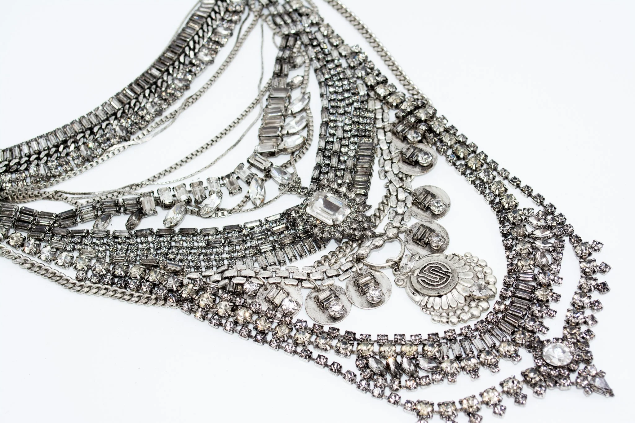 Multiple layered silver and clear rhinestone necklaces on a white background.