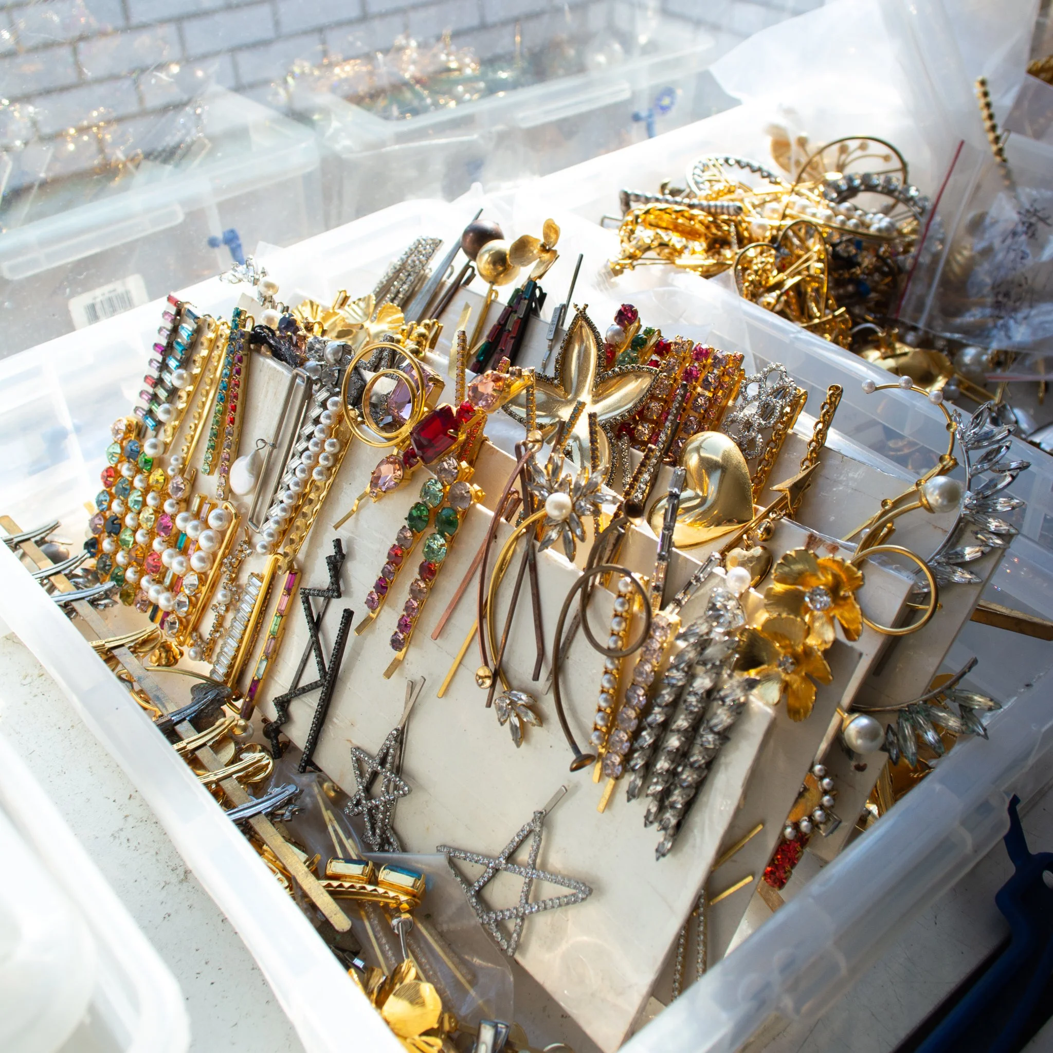 Collection of assorted jewelry including earrings, hairpins, and decorative accessories, arranged in a plastic container with various sections.