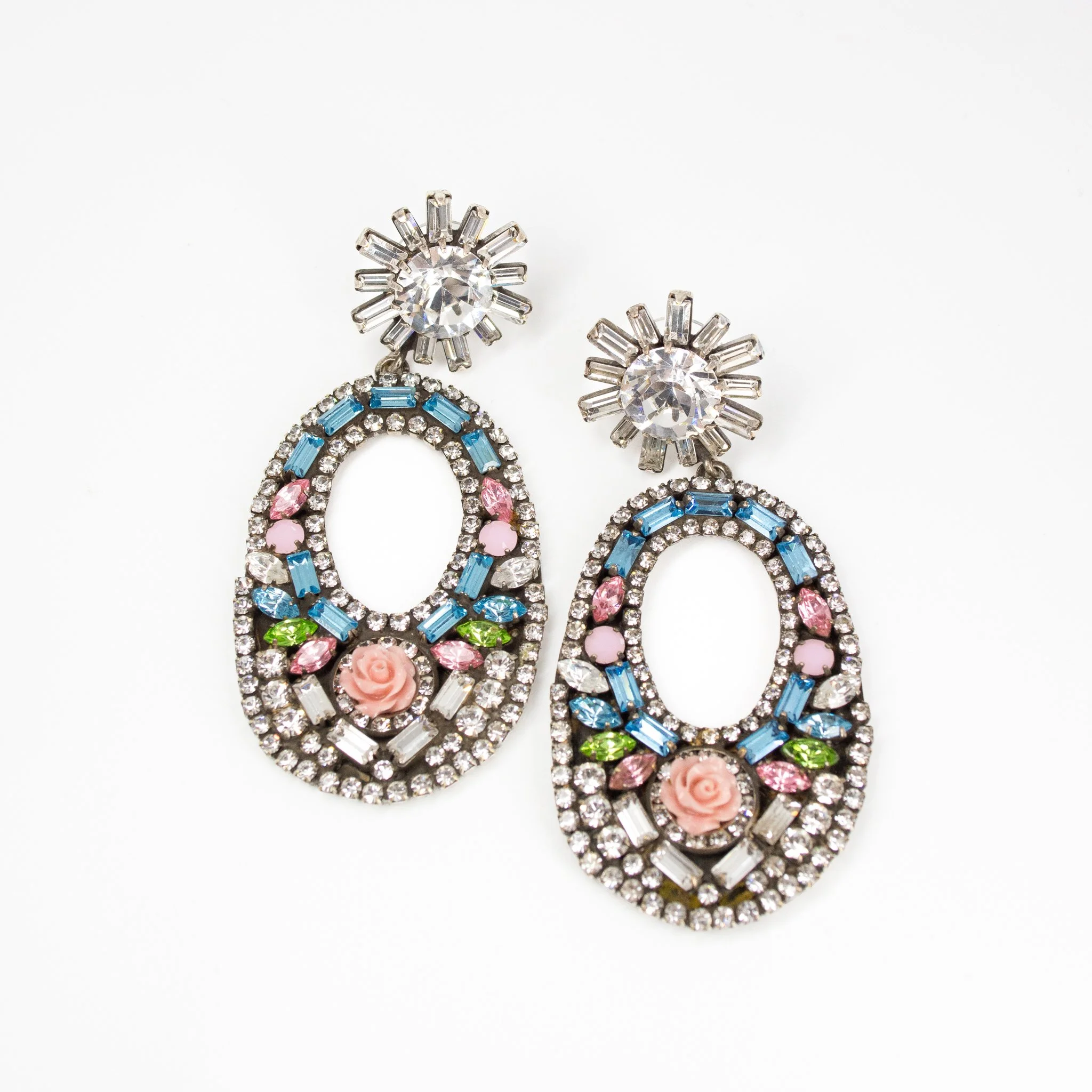 Pair of decorative earrings with flowers, pink roses, and colored gemstones surrounded by clear rhinestones on a white background.