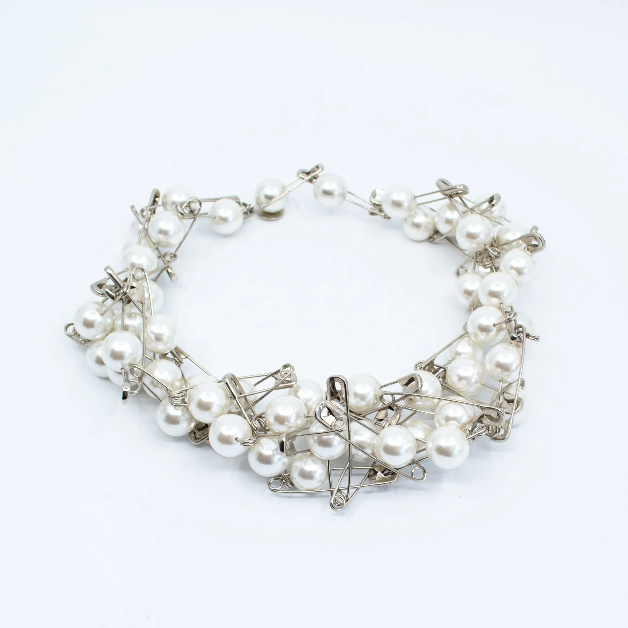 Bracelet made of safety pins and white pearls, arranged in a circular shape on a white background.