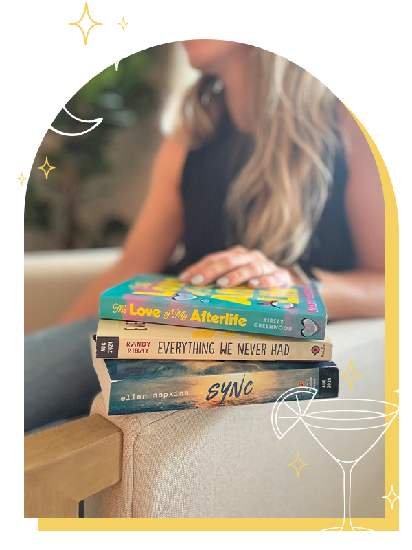 A woman with long hair is sitting on a couch behind a stack of three books on a wooden table. The books are titled 'The Love of My Afterlife', 'Everything We Never Had', and 'Sync'. The image has a decorative yellow border with white and yellow star and moon illustrations.