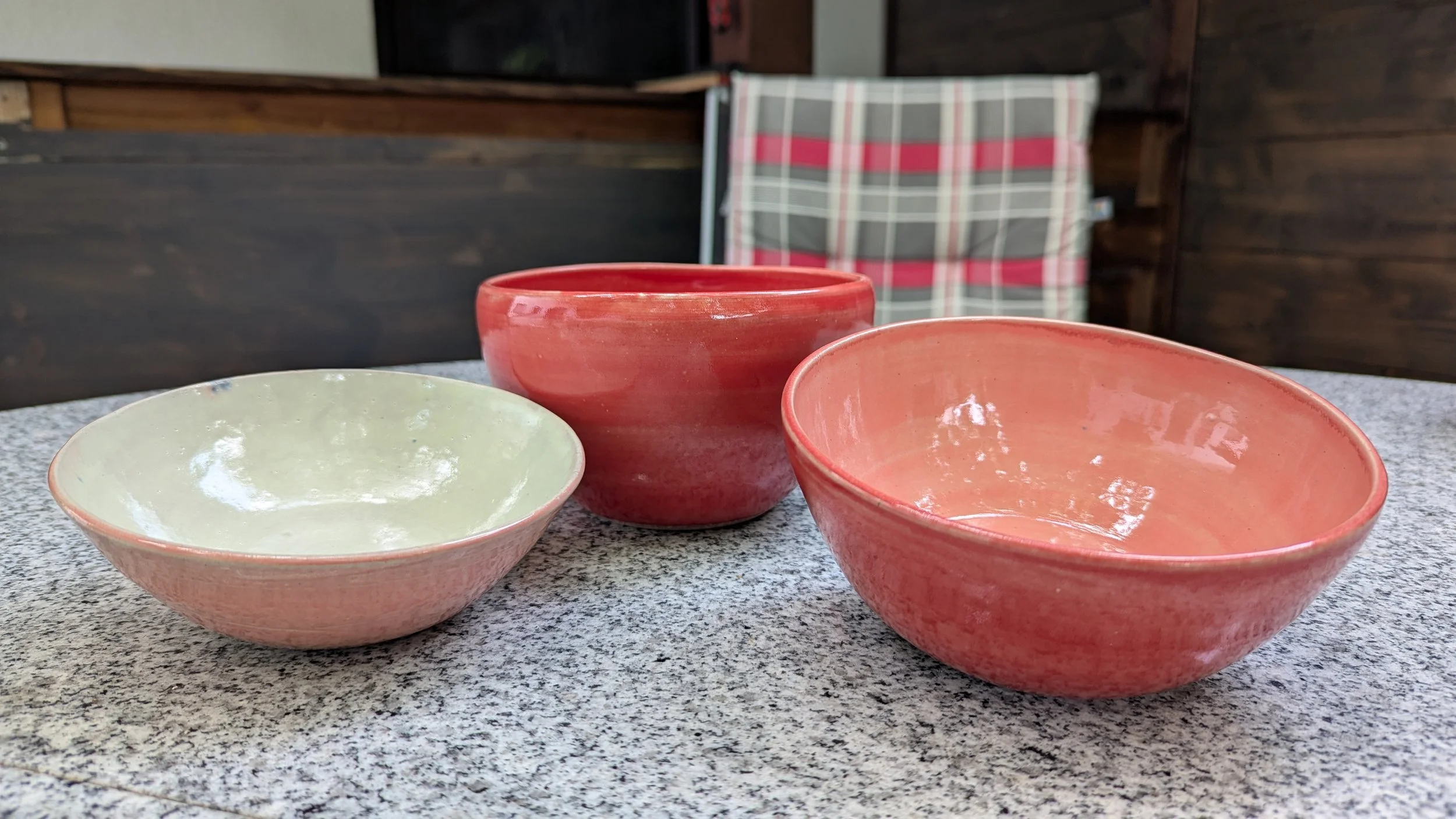 Drei Keramikschalen in Pastellfarben auf einer Tischplatte. Im Hintergrund eine Sitzgelegenheit mit kariertem Bezug.