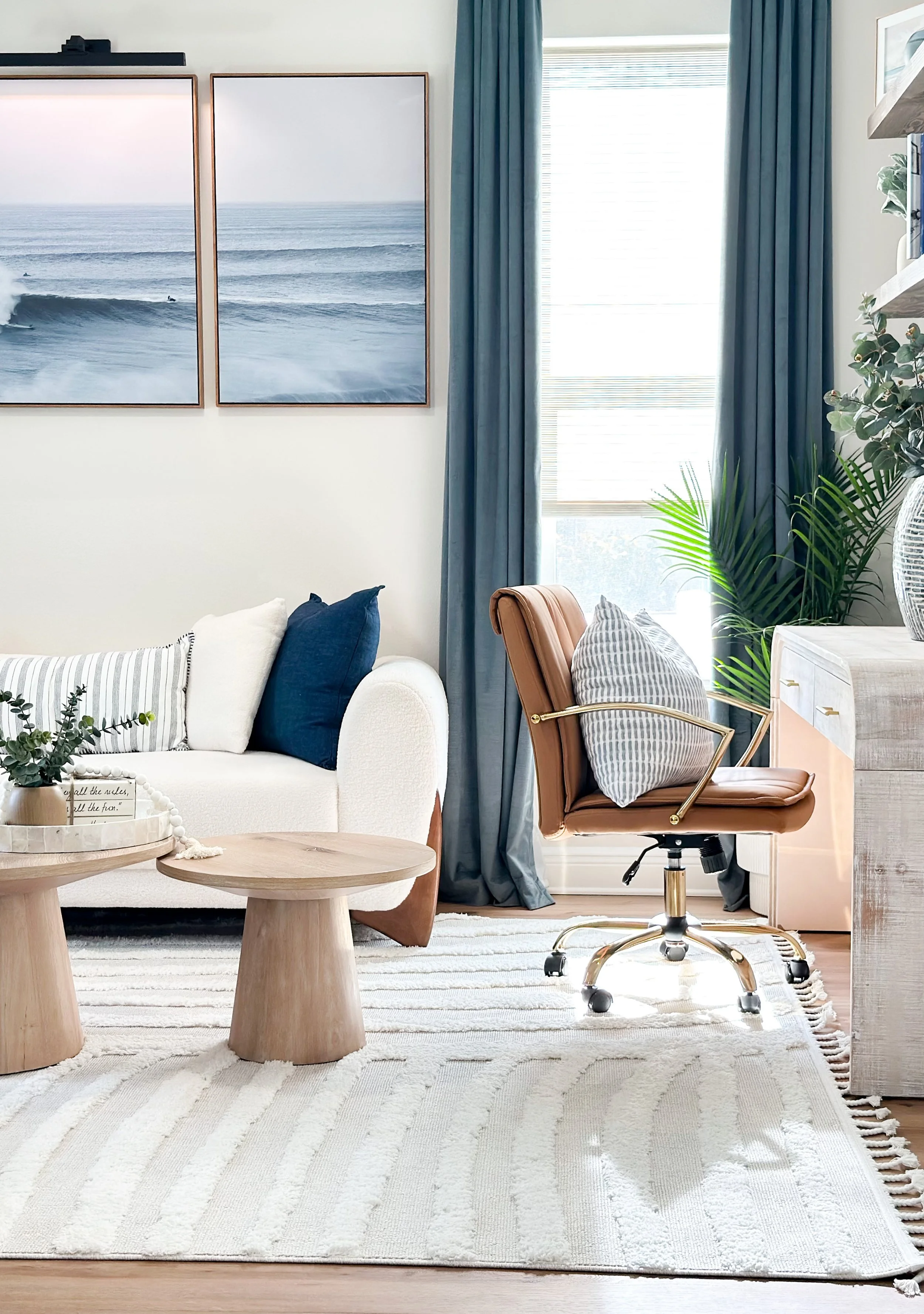 Tampa Bay interior design, id Designs & Co., seating area with beach themed furniture, white sofa with blue pillows, office chair, with wooden desk, wooden tables, beige rug, blue curtains with wooden roller shades, beach themed wall art.