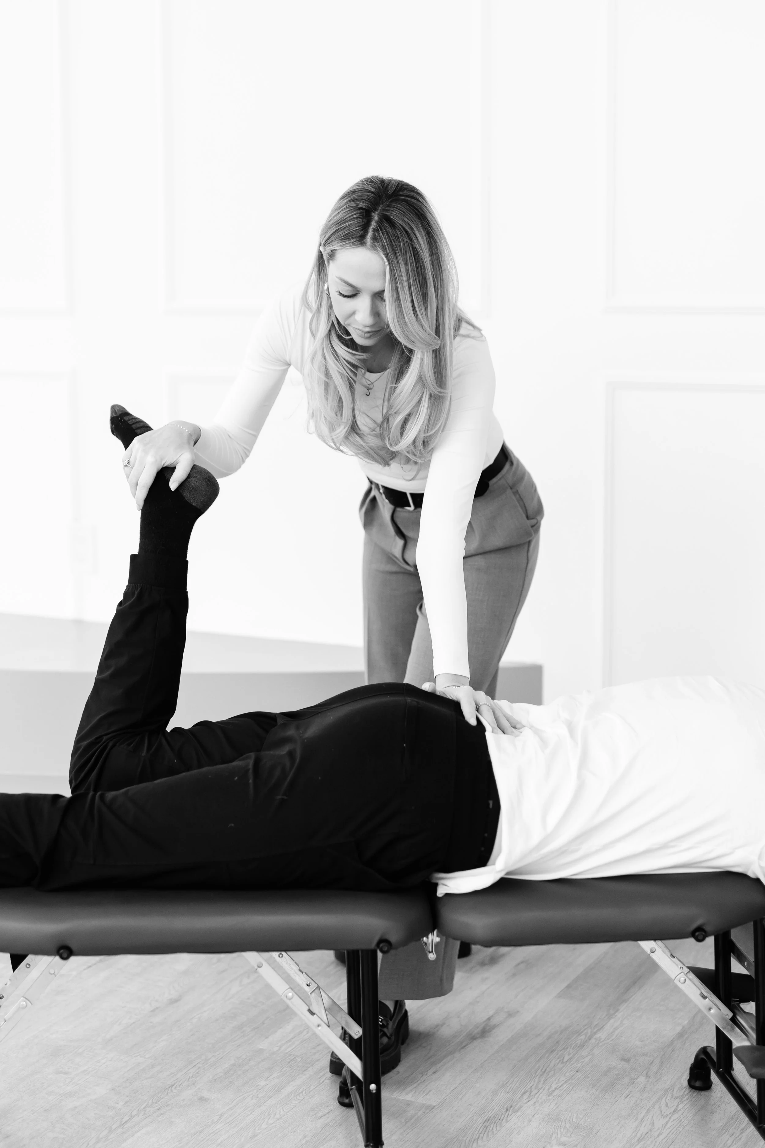 Black massage or chiropractic table with a gray device on top, in a room with light-colored wooden floor.