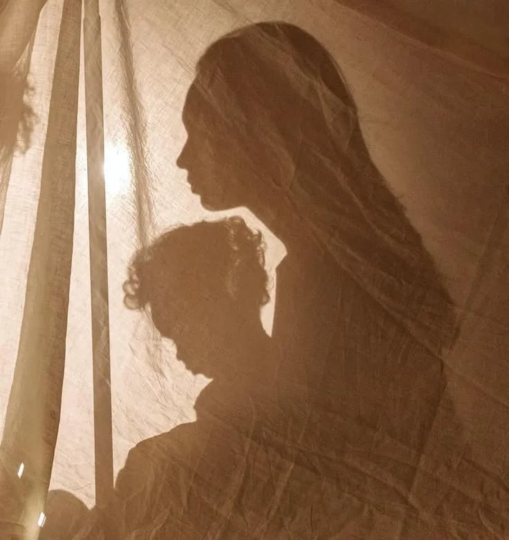 Ombre silhouette d'un enfant assis sur les genoux de sa maman derrière un drap beige