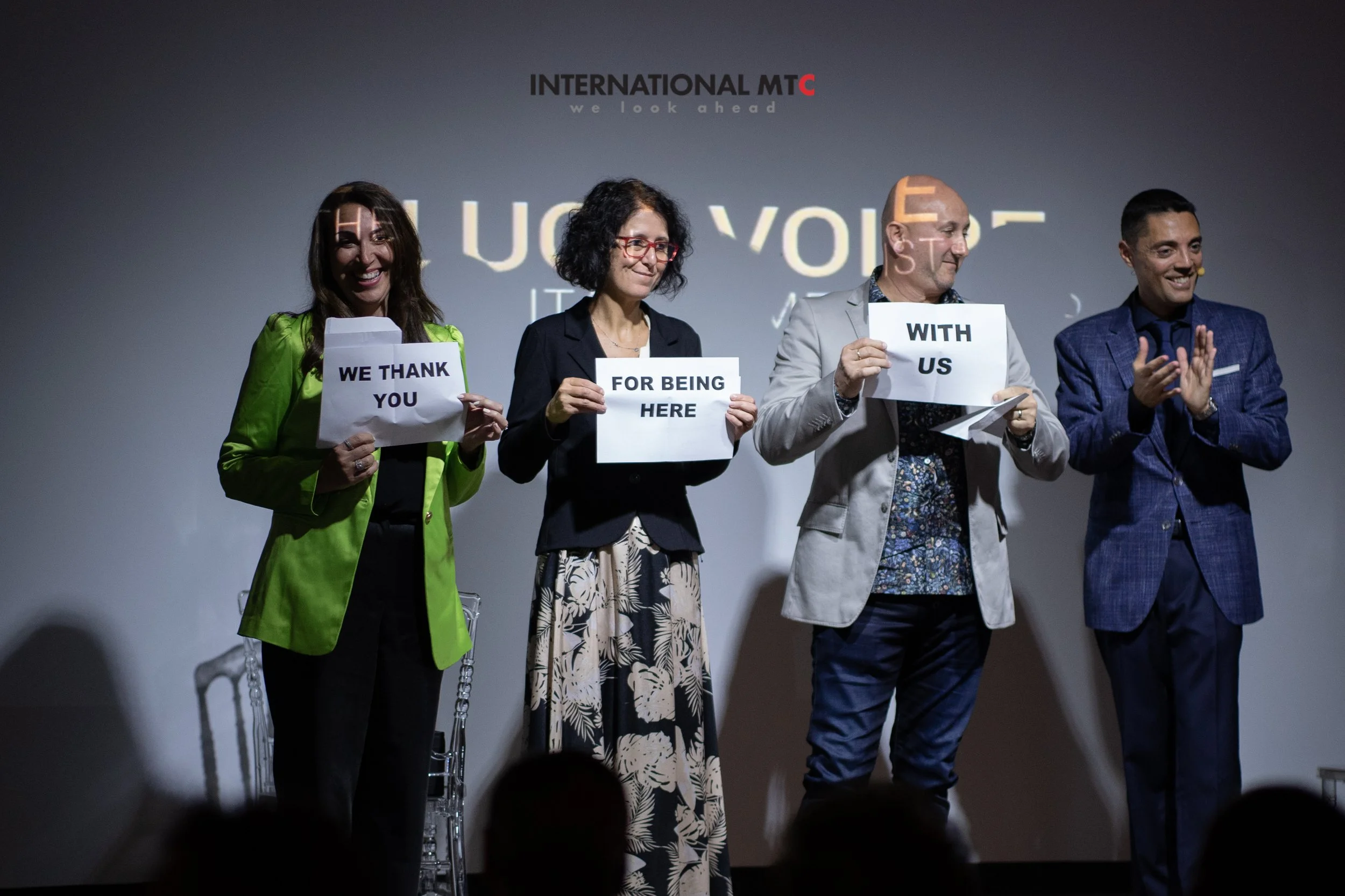 Four people standing on a stage smiling and clapping.