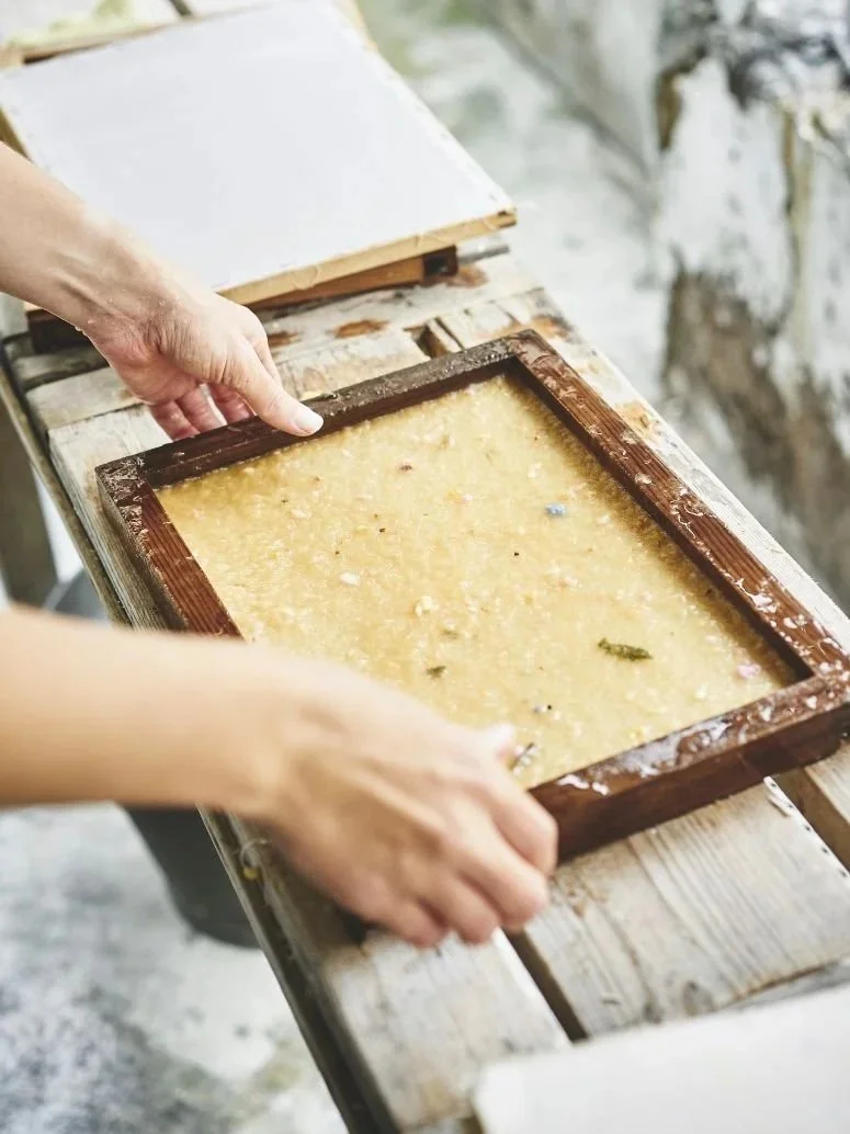 Person using a wooden frame to make cheese on a wooden table outdoors.