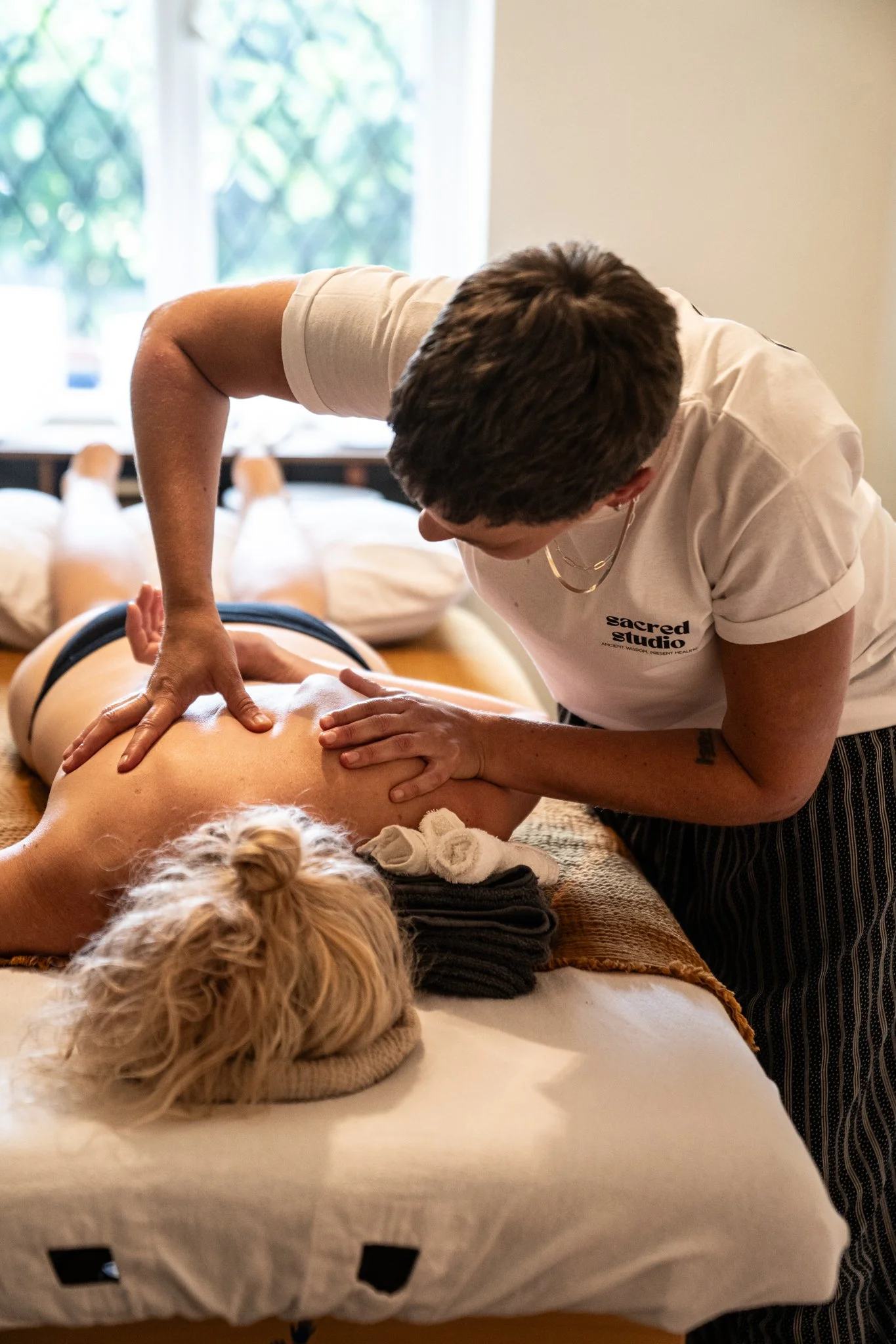 A massage therapist giving a massage to a woman lying face down on a massage table.