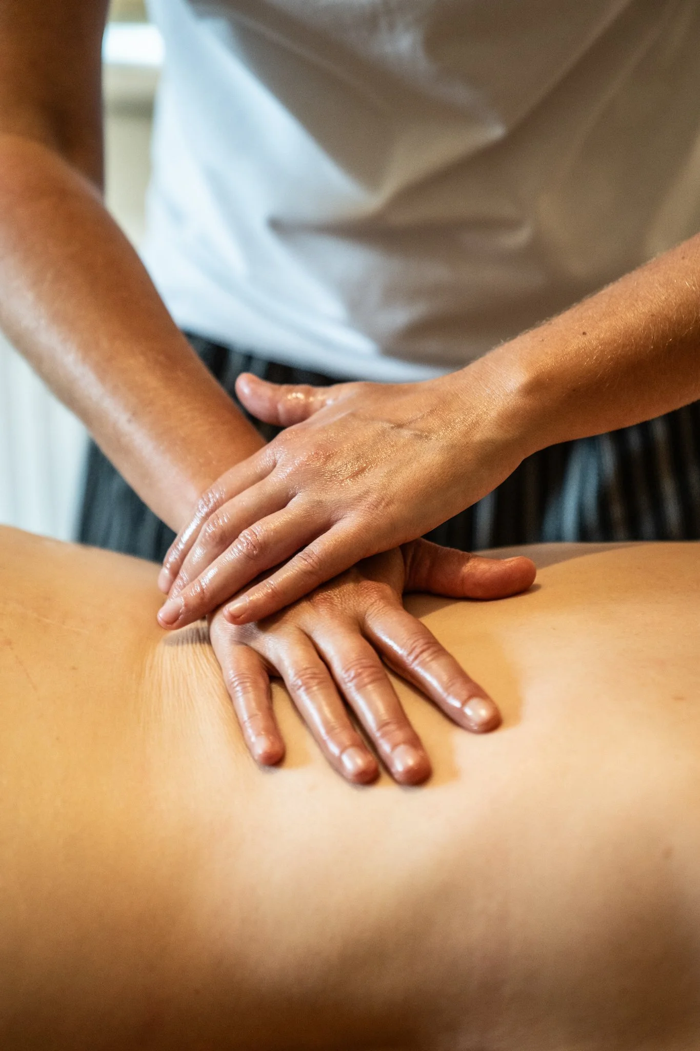 A massage therapist's hands applying massage oil on a person's back during a massage therapy session.