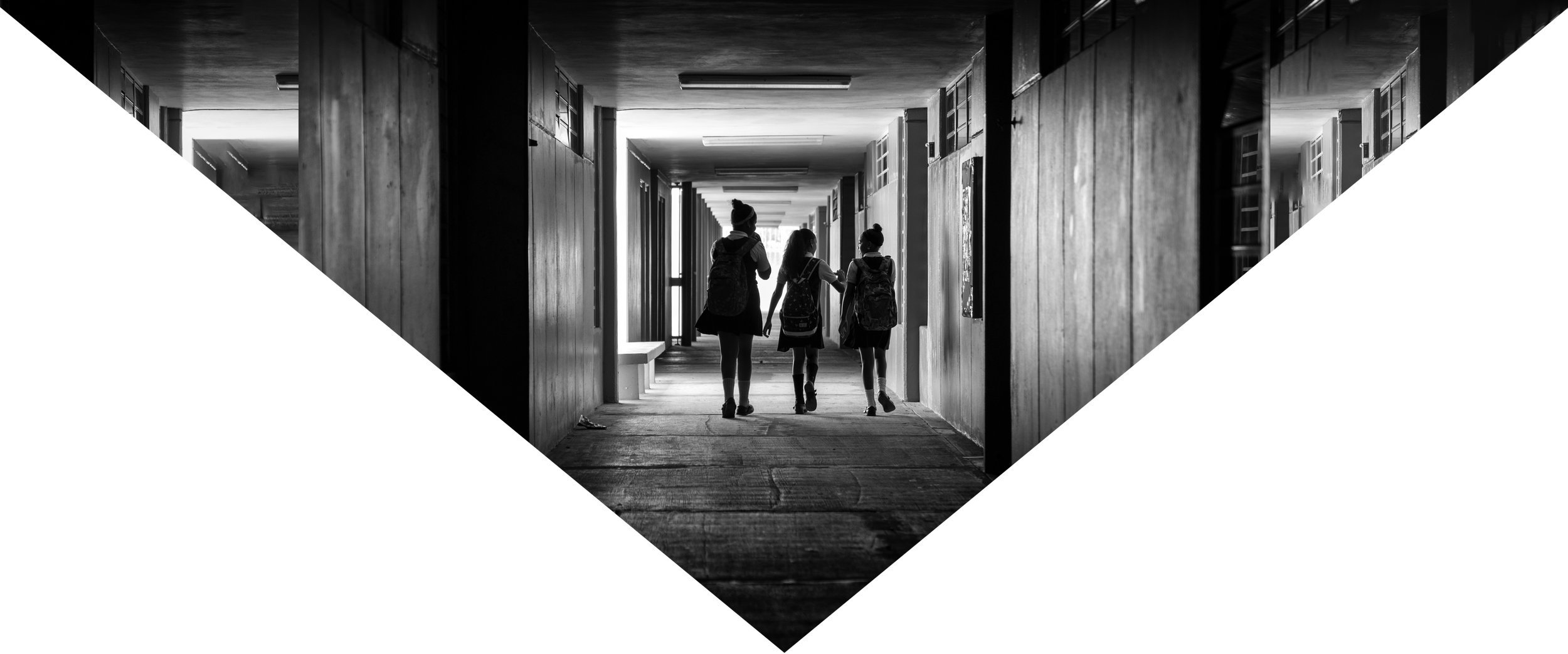 Jóvenes con mochilas caminando por un pasillo interior de un edificio, vista en blanco y negro.