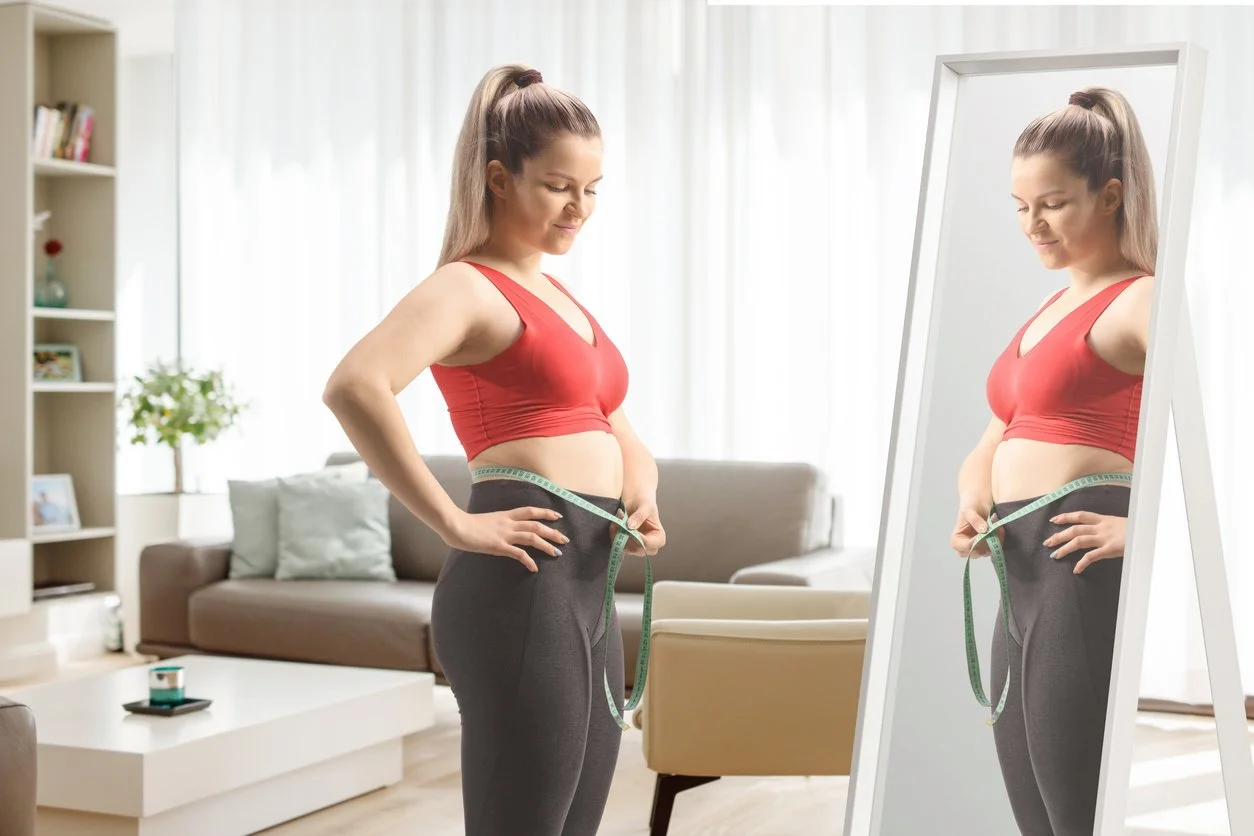 Young woman in front of a mirror measuring her waist with body measuring tape