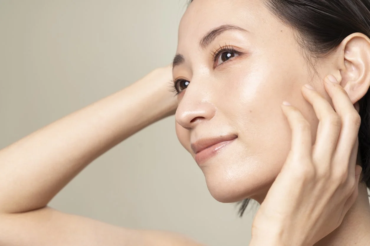 Asian woman looking to the side with hands up near face showcasing smooth skin
