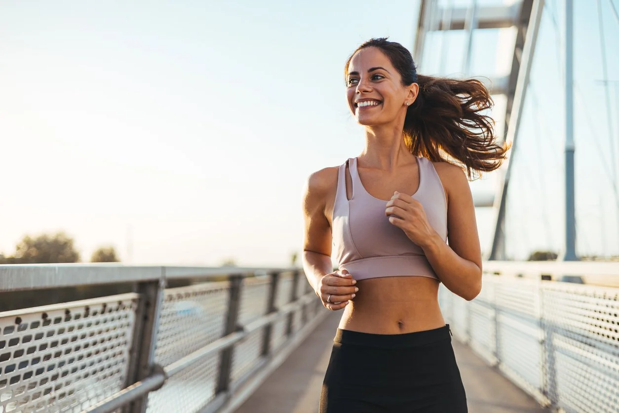 Young woman smiling while going for a run on a bridge