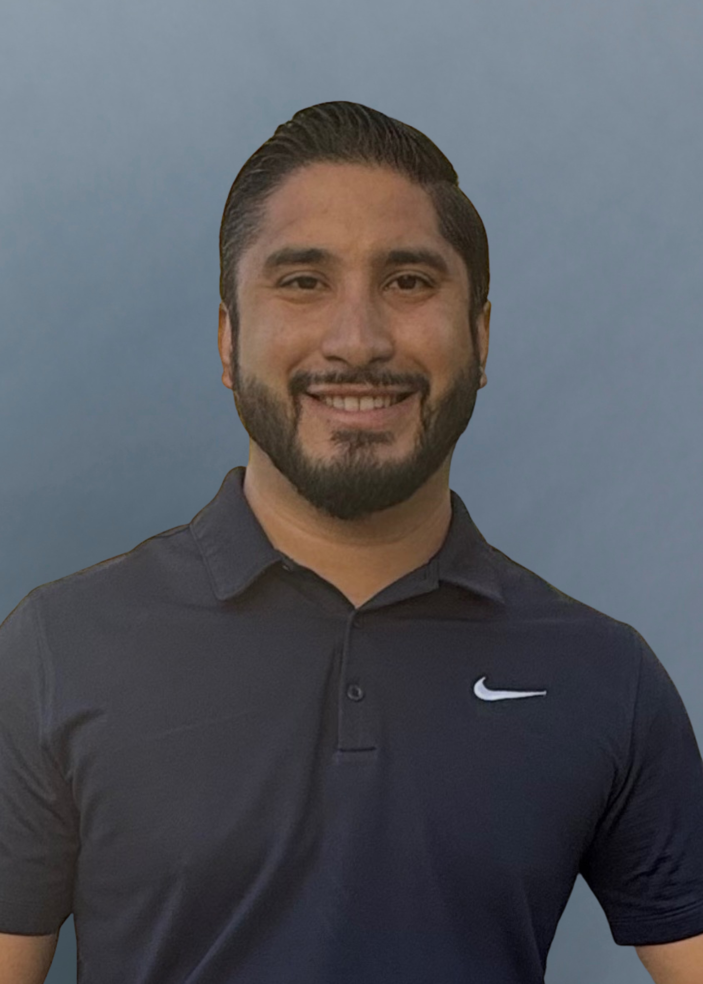 A smiling man with a beard, wearing a black Nike polo shirt, standing in front of a foggy or cloudy sky.