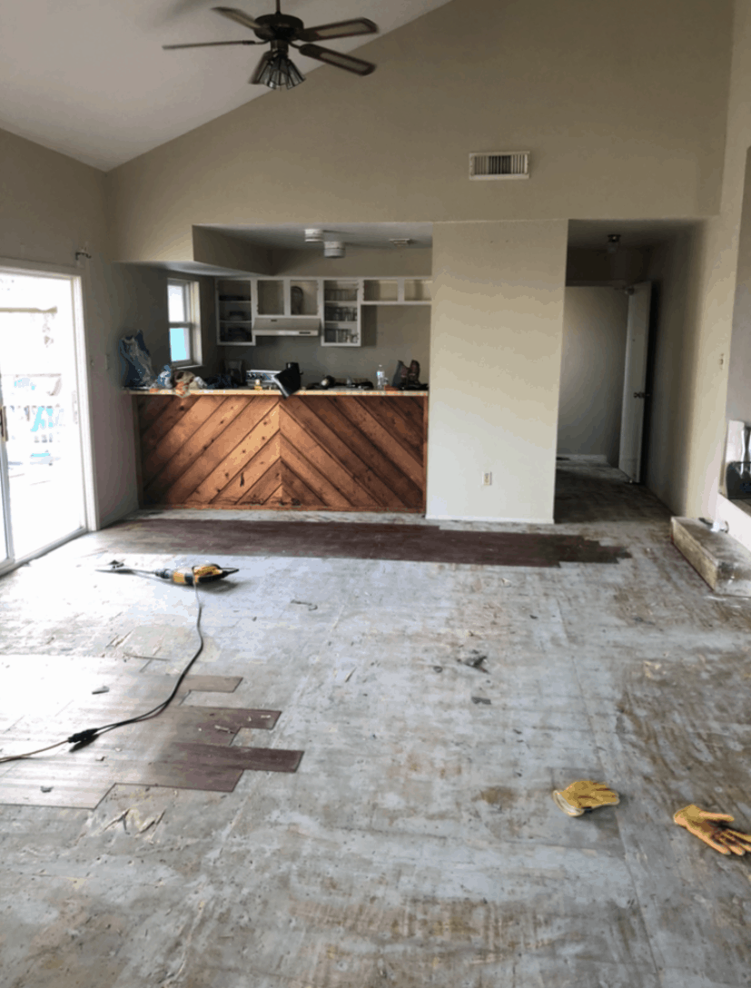 Interior of a room under renovation with partially removed flooring, a ceiling fan, a wooden bar, and some construction tools.