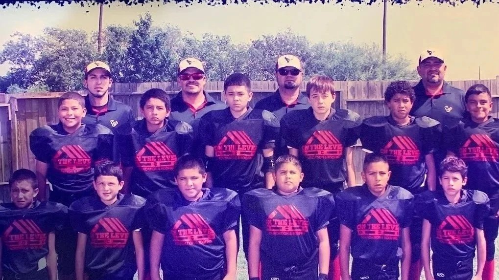 A youth football team with coach and assistant coach posing outdoors in uniform.