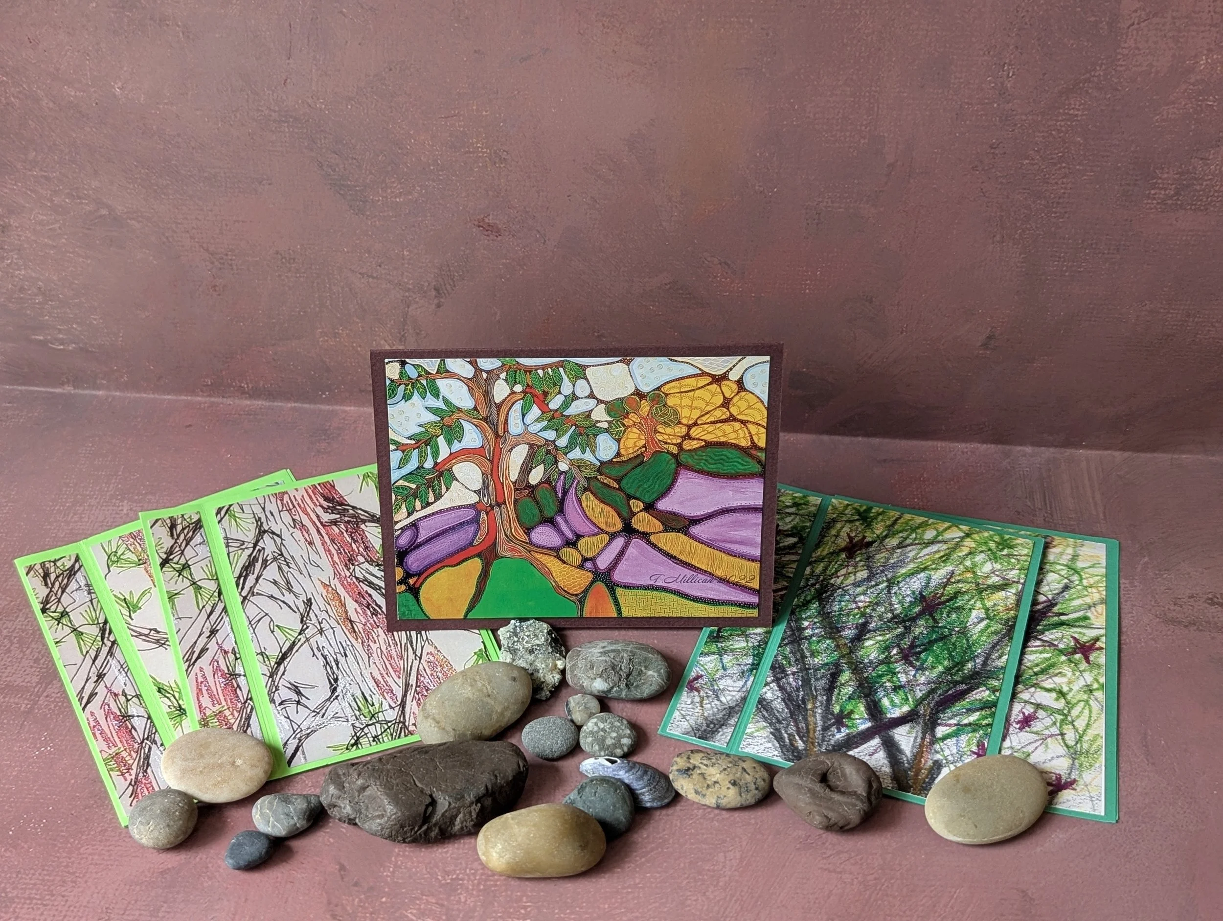 Colorful artwork prints featuring trees and landscapes surrounded by rocks on a pink surface.