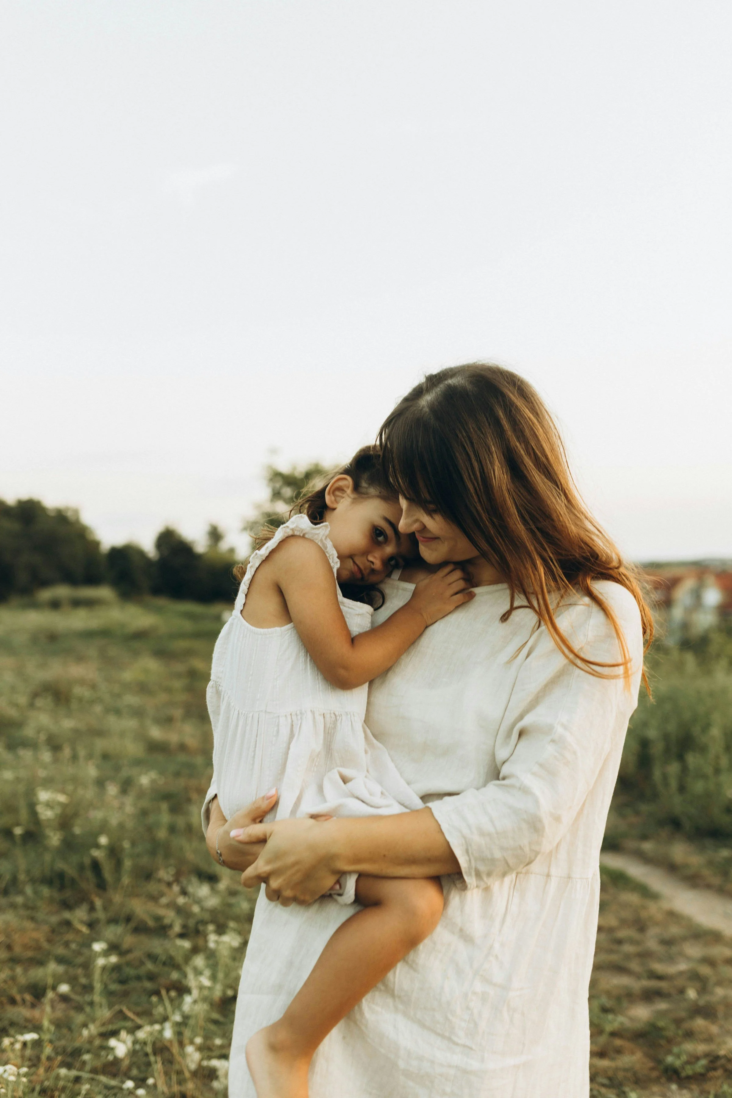 A woman holding a young girl in a field during sunset.