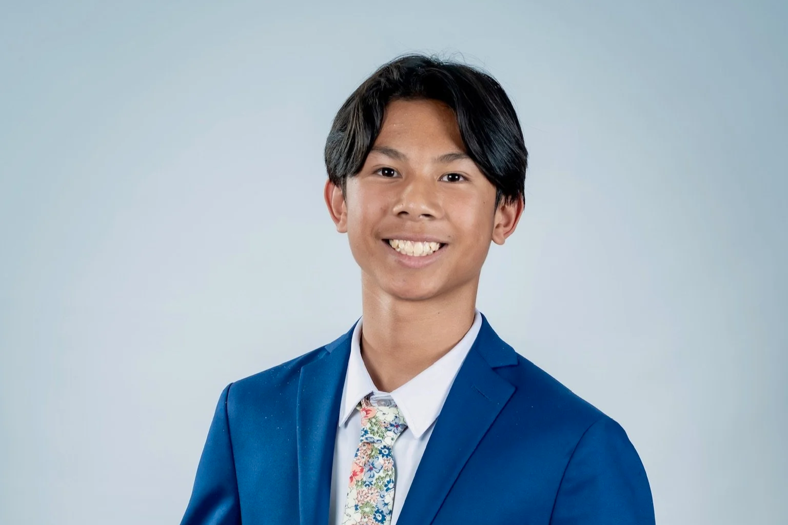 Smiling young man in a blue suit, white shirt, and floral tie against a light blue background