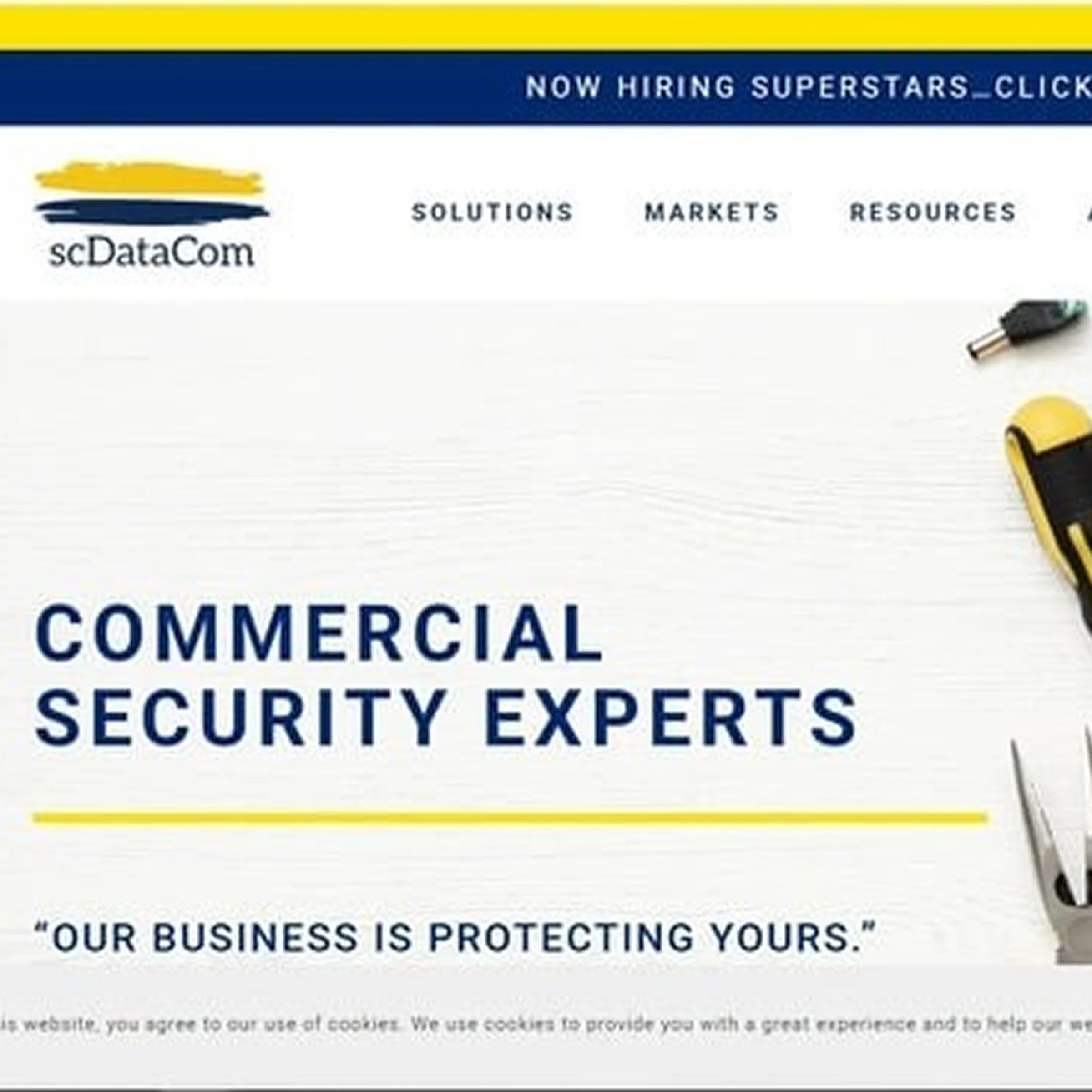 Website homepage for sCDatCom with the headline 'Commercial Security Experts' and a tagline 'Our business is protecting yours.' The top navigation menu includes links to Solutions, Markets, Resources, and a notice about hiring superstars.