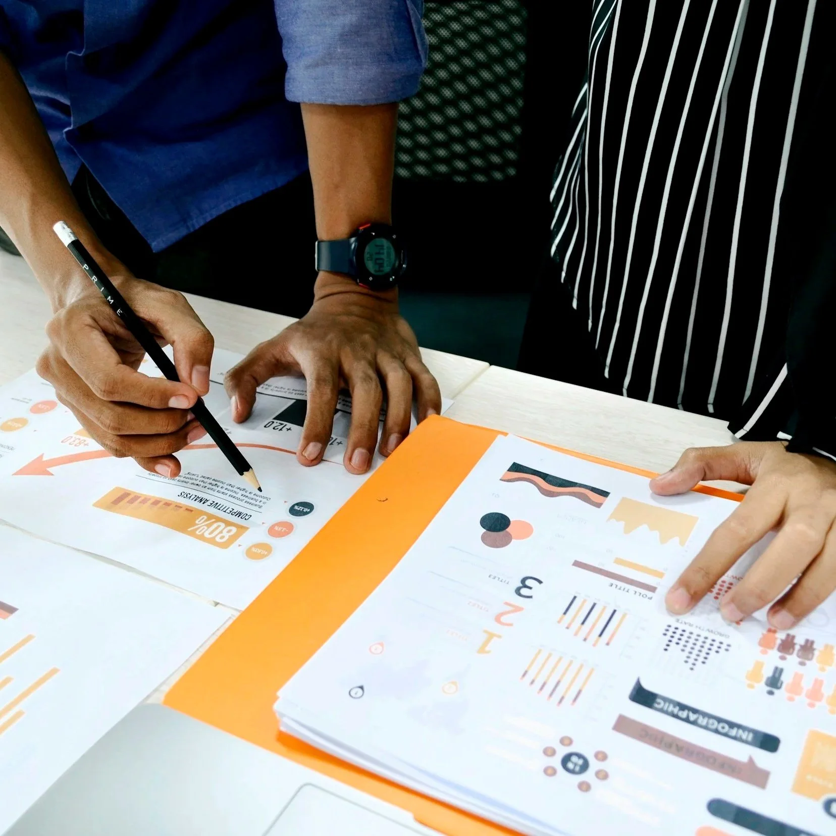 Two people holding pencils making marks on graphs laid on a table