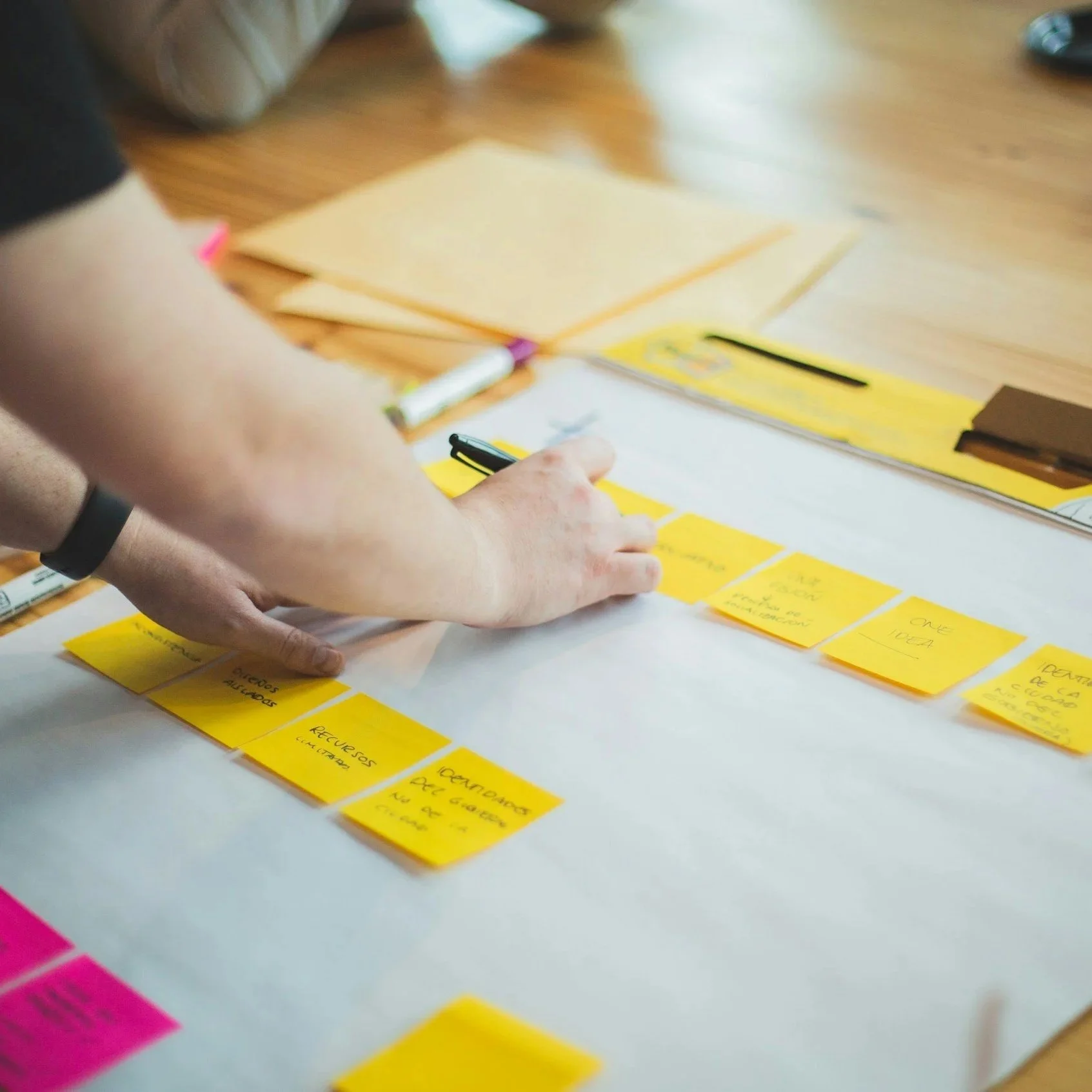 Person writing on a sticky note in line with several other sticky notes pasted on a board