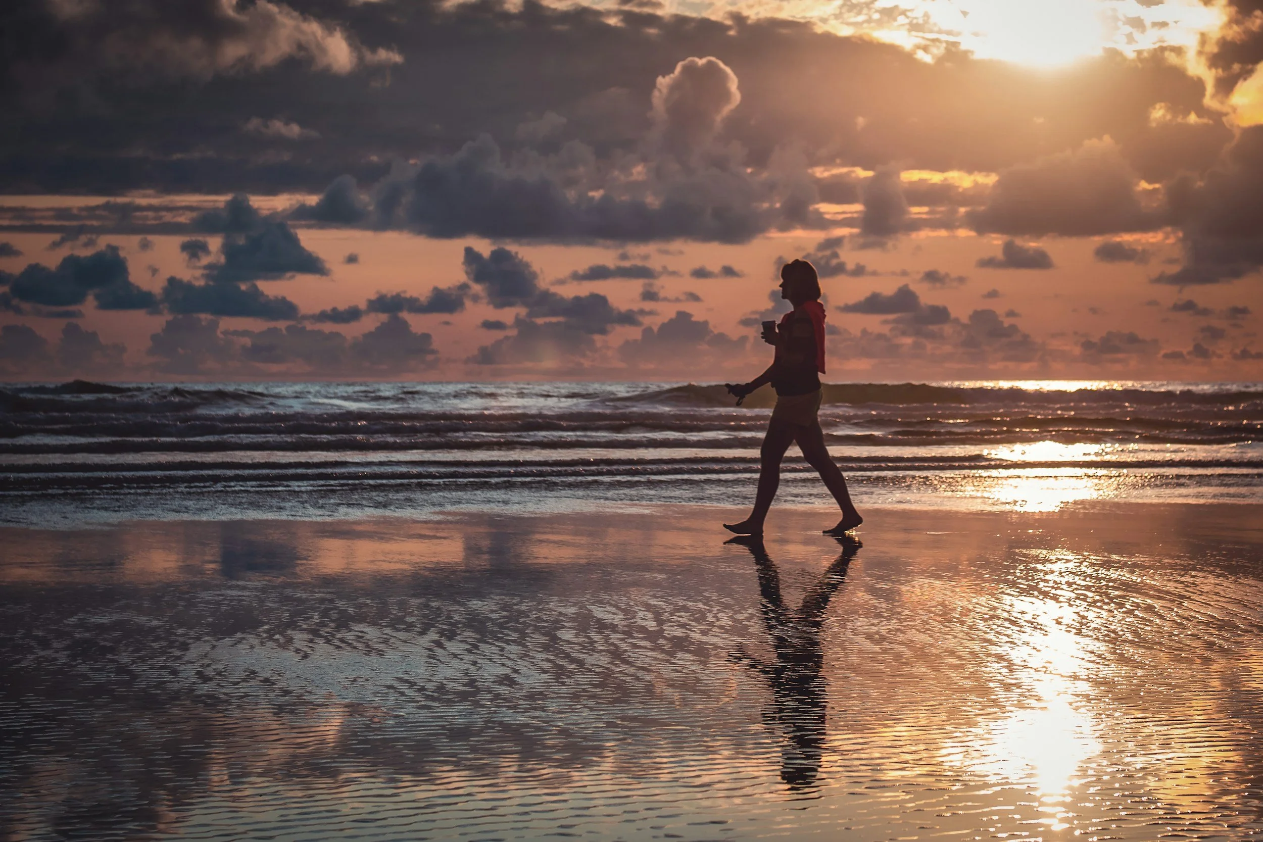 High-achieving woman walking on the beach at sunrise who is ready to overcome people-pleasing and build healthier boundaries.