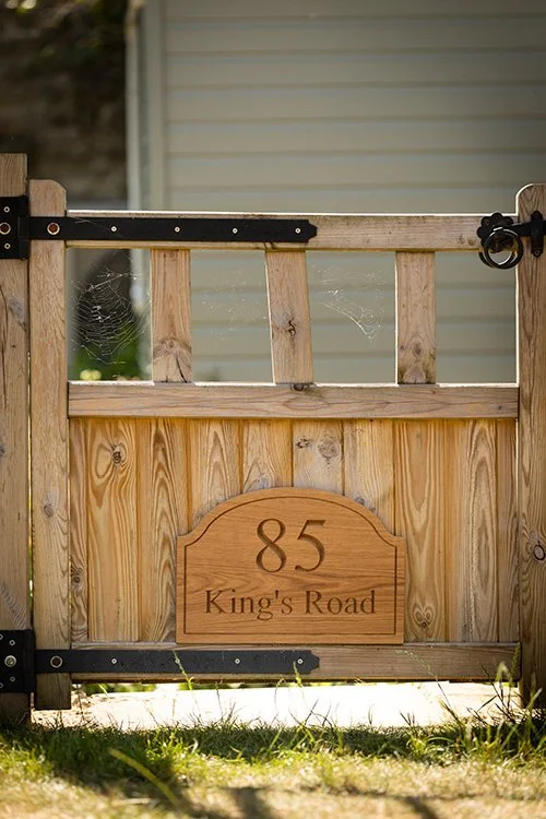 Wooden gate with a house number 85 and street name 'King's Road' engraved on a wooden plaque, with spider webs visible on the gate.