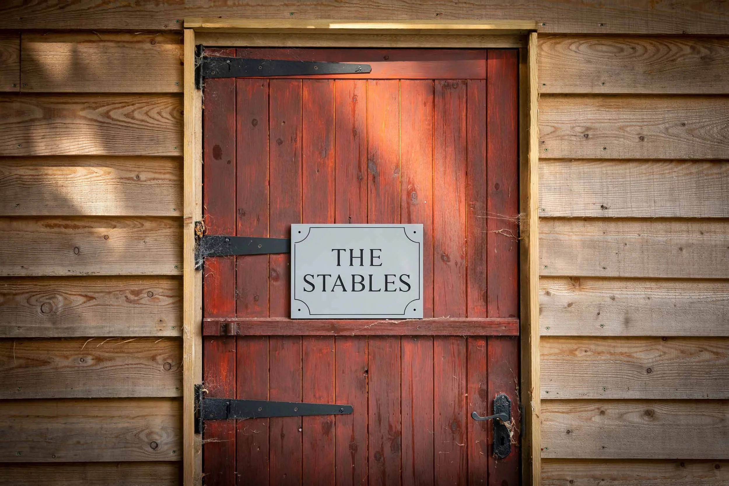 Red wooden barn door with black hardware and a sign that reads "The Stables" mounted on it.