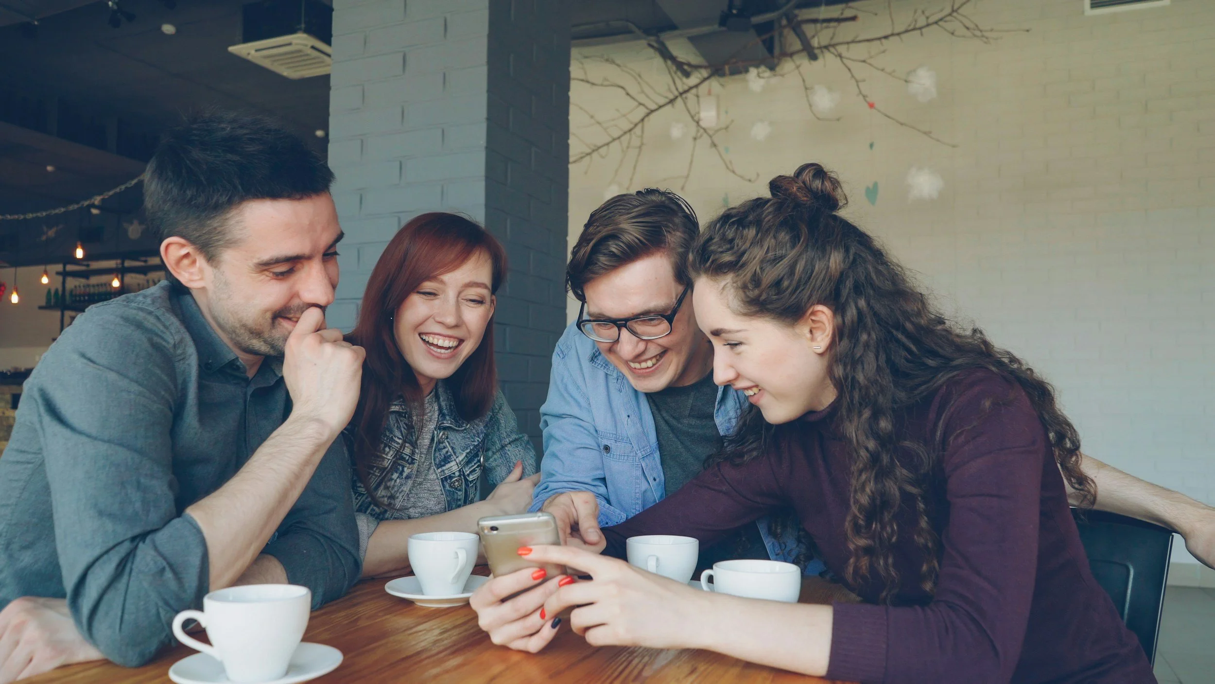 Group of men and women at table with coffee looking at phone smiling