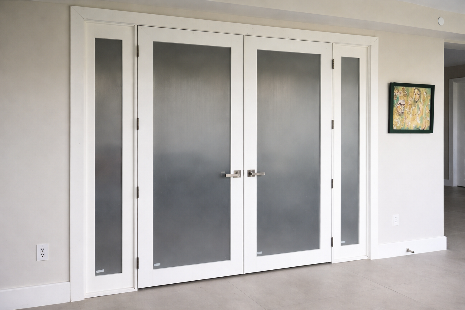 Set of white-framed double doors with frosted glass panels in a modern home interior, accompanied by a small painting on the wall to the right.
