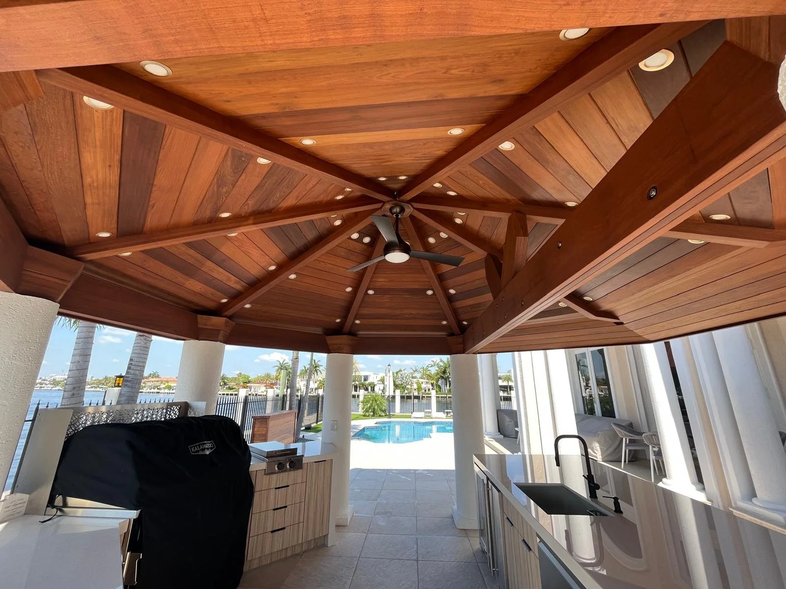Outdoor patio with wooden ceiling, ceiling fan, and view of swimming pool and waterway in the background.