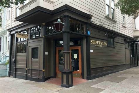 Corner of a building with black siding, a wooden door, and signs reading 'Shotwell's' and 'Shotwell's Bar & Grill'.
