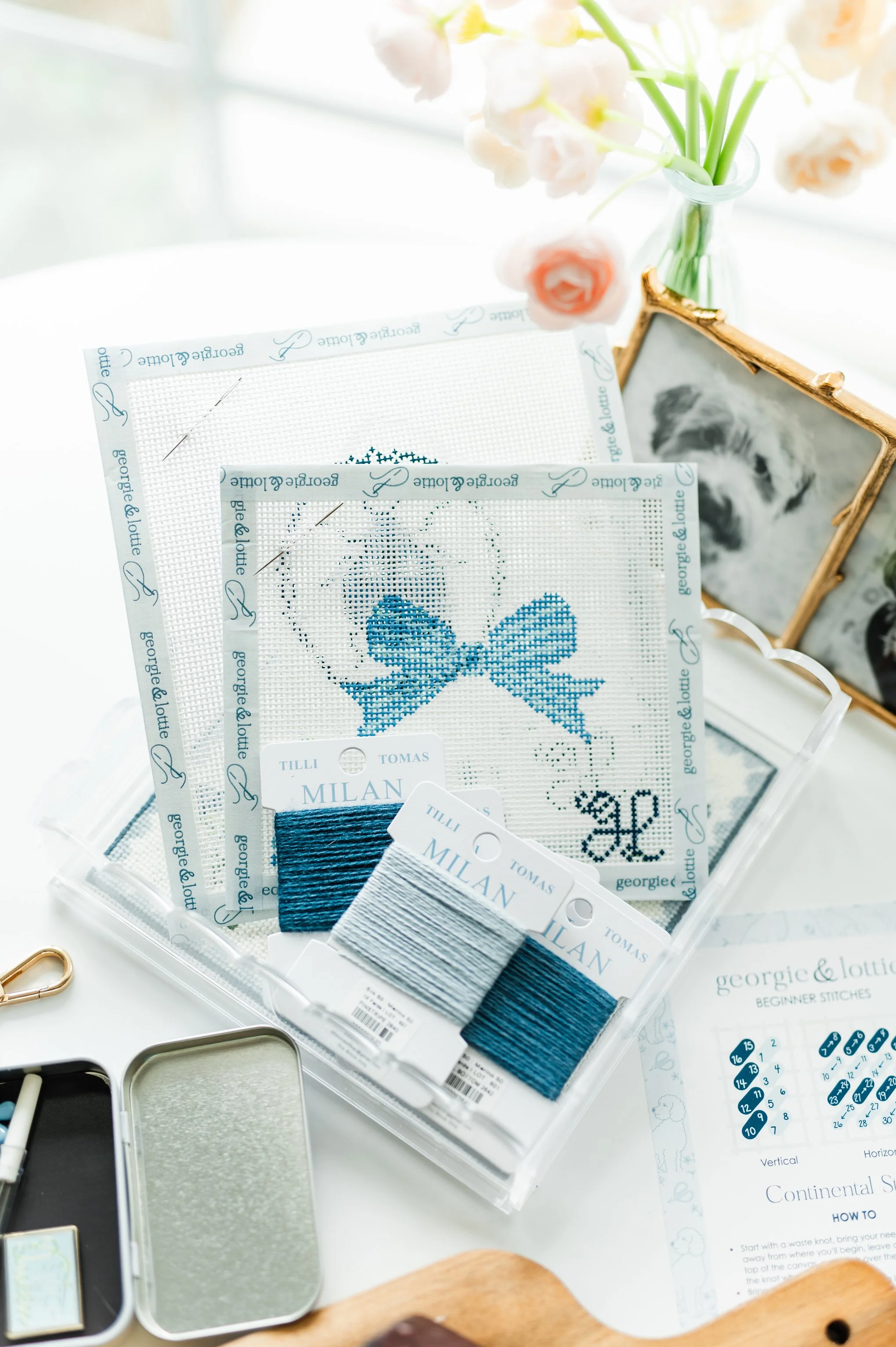 A collection of embroidery floss, cross-stitch patterns, a framed photo, and sewing accessories on a white surface.